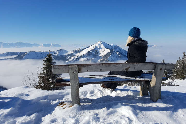 Frau blickt am Ende Ihrer Winterwandertour vom Gipfel auf die Schneelandschaft hinab