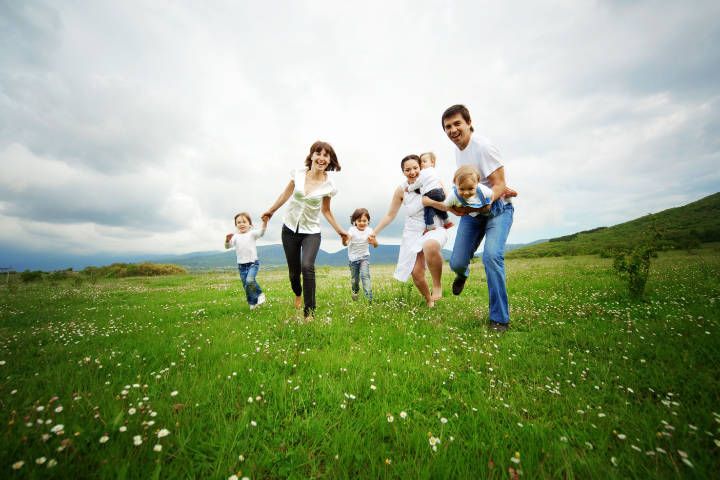 Eltern laufen gemeinsam mit deren Kindern über eine Blumenwiese