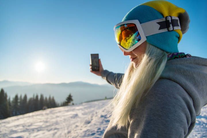 Frau macht beim Skifahren ein Selfie mit Sonnenuntergang im Hintergrund