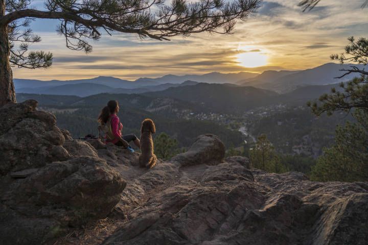 Frau genießt nach einem Wandertag den Sonnenuntergang mit ihrem Hund